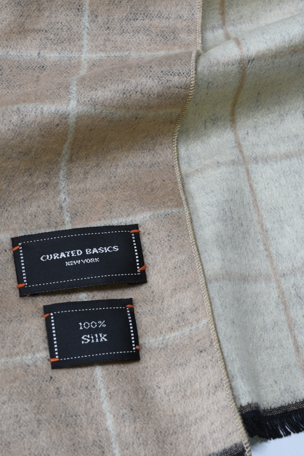 Label on a checkered fabric with 'Curated Basics New York' and '100% Silk' text.