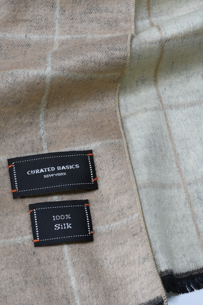 Label on a checkered fabric with 'Curated Basics New York' and '100% Silk' text.